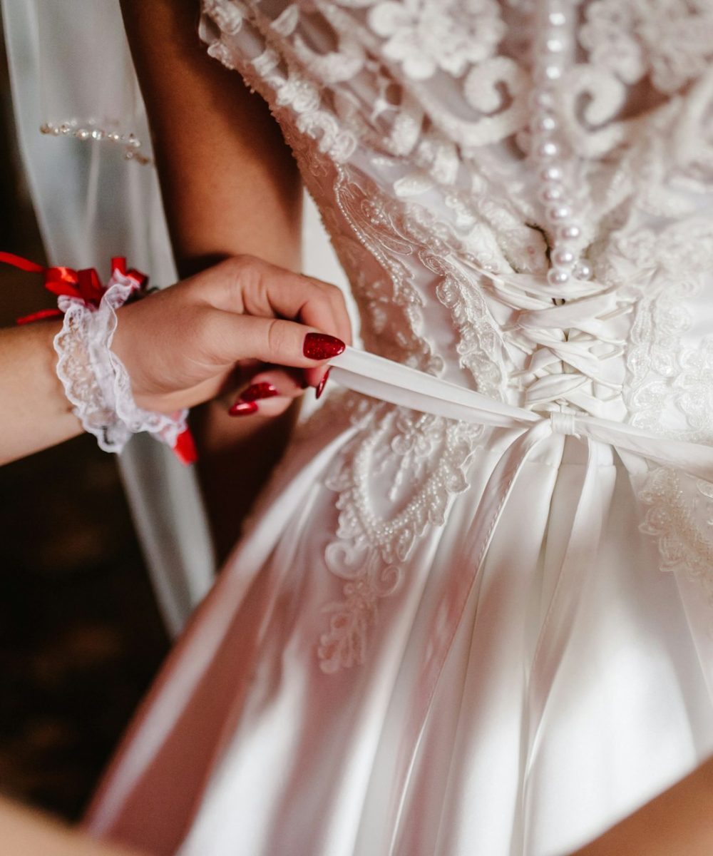 Bridesmaid helping bride fasten corset and getting her dress, preparing bride in morning for