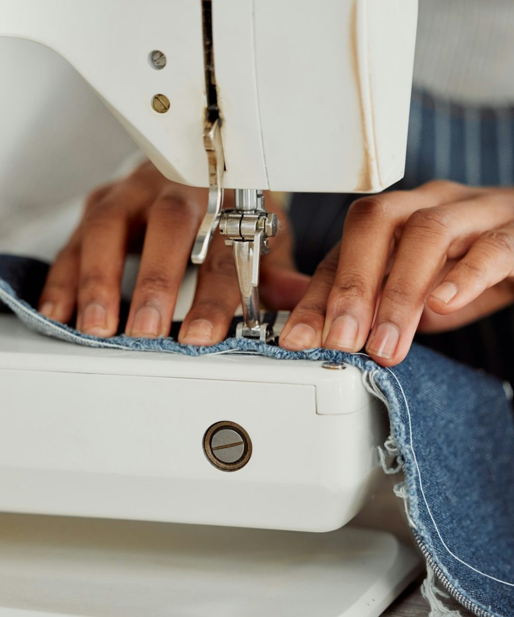 Close up hands of a professional seamstress female sitting on a white sewing machine in her studio.